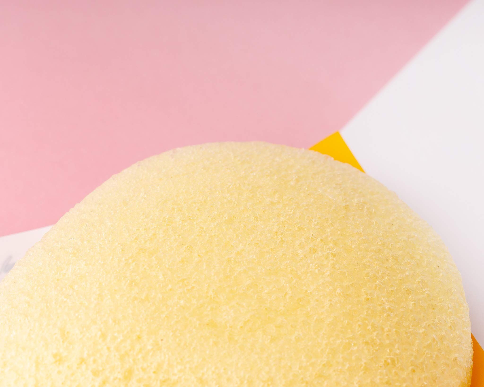 Gelber Schwamm, rundlich, auf rosa und weißem Hintergrund. Textur mit kleinen Poren.