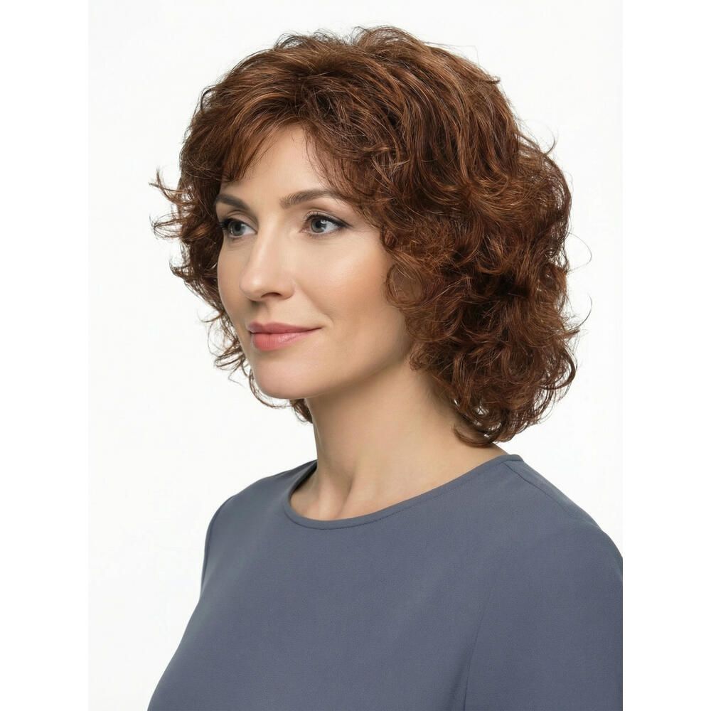 Frau mit brauner, lockiger Perücke. Sie trägt ein graues Oberteil. Der Hintergrund ist weiß.