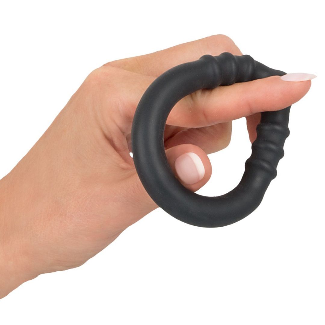 Ein schwarzer Penisring aus Silikon, gehalten von einer Hand. Der Ring hat eine geriffelte Textur und eine erhabene Spitze.