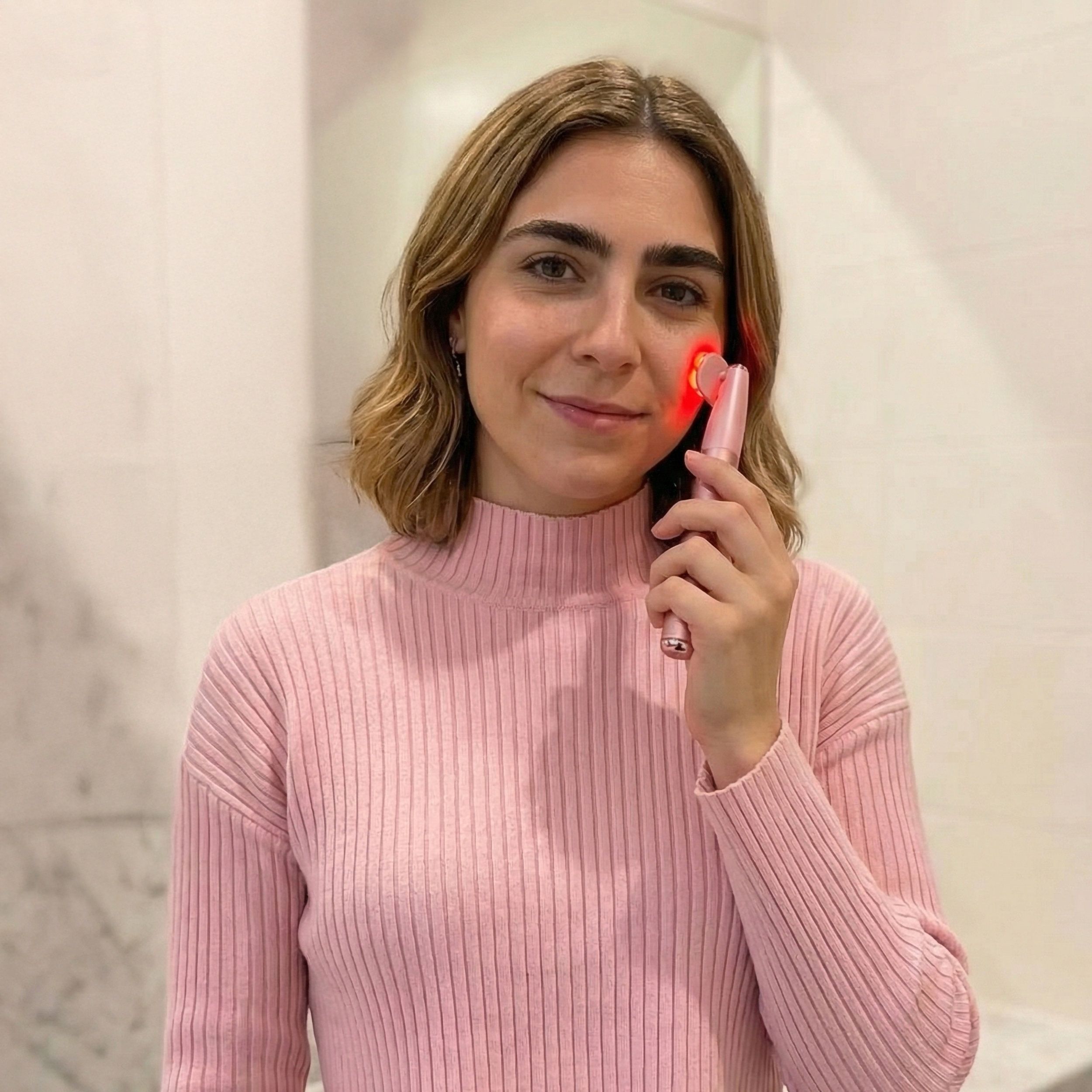 Eine Frau benutzt ein rosa RF EMS LED Anti-Aging-Gerät im Gesicht.