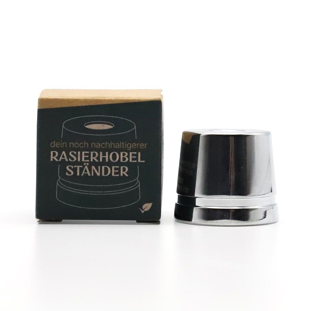 Verchromter Rasierhobel-Ständer neben Verpackung. Verpackung mit Text: Rasierhobel Ständer. Ständer aus Metall, zylindrisch.