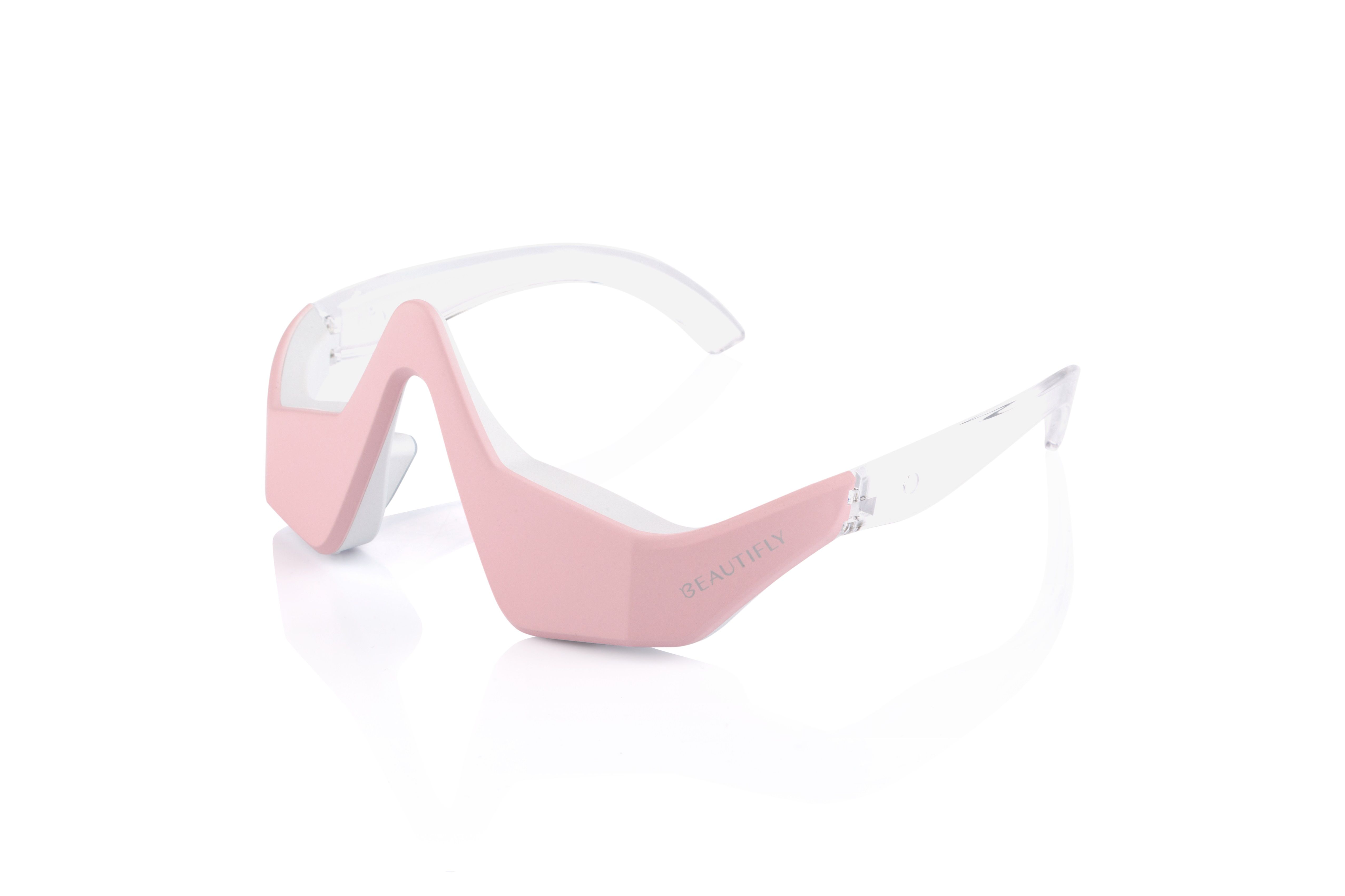 Rosa Augenmassagegerät in Brillenform. Transparente Bügel. Produktname auf dem Bügel.