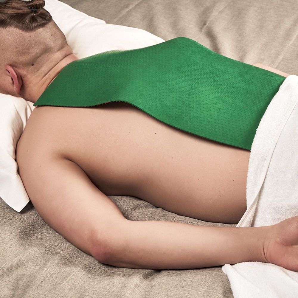 Mann liegt auf dem Bauch, ein grünes Produkt auf dem Rücken. Der Rücken ist bedeckt.