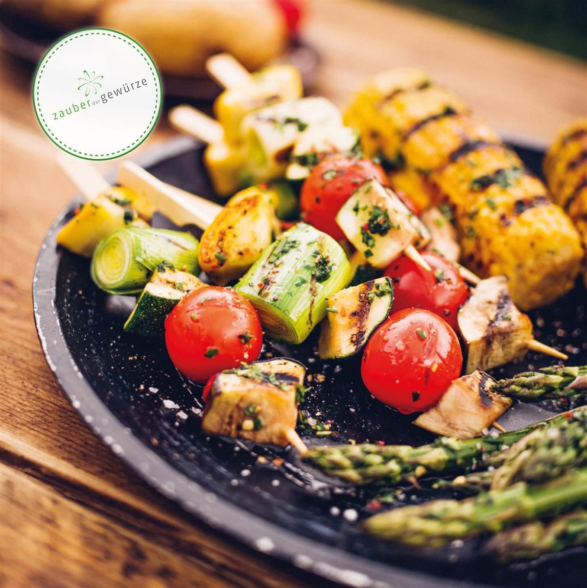 Gegrilltes Gemüse auf Spießen, serviert auf einem schwarzen Teller. Mais, Tomaten, Zucchini und Spargel.