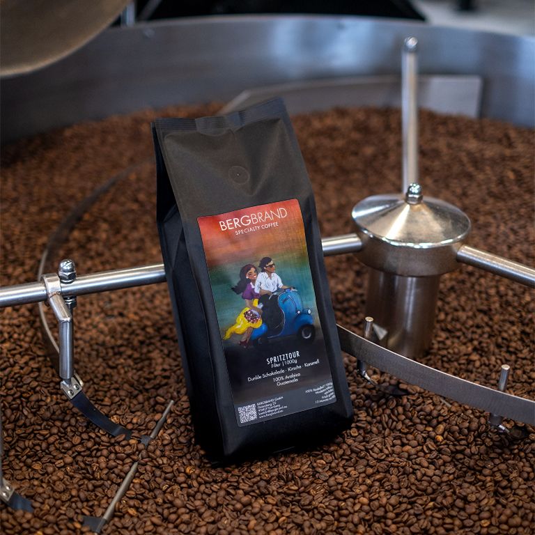 Schwarzer Beutel mit BERGBRAND-Logo und Illustration. Kaffeebohnen im Hintergrund. Text: Spritztour, Specialty Coffee.