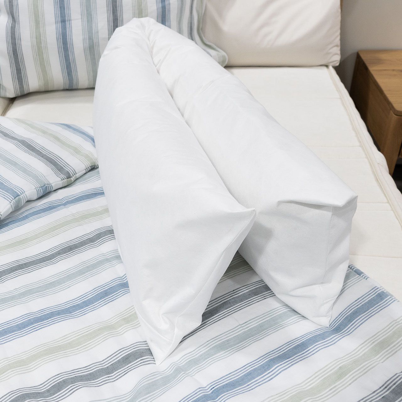 Weißes Seitenschläferkissen auf einem Bett. Kissen in V-Form, auf gestreifter Bettwäsche.