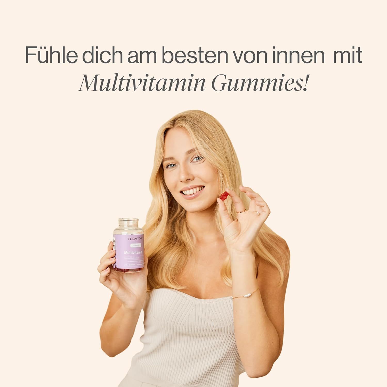 Frau hält eine Flasche TummyTox Multivitamin Gummibärchen und ein Gummibärchen. Sie lächelt.