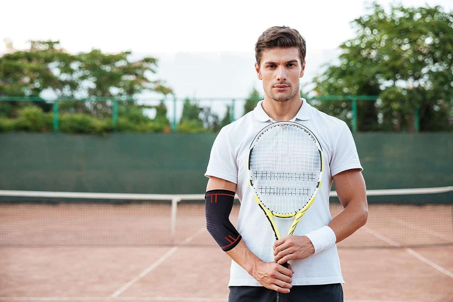 Mann mit Tennisschläger und Ellbogenbandage. Steht auf einem Tennisplatz. Sportbekleidung.