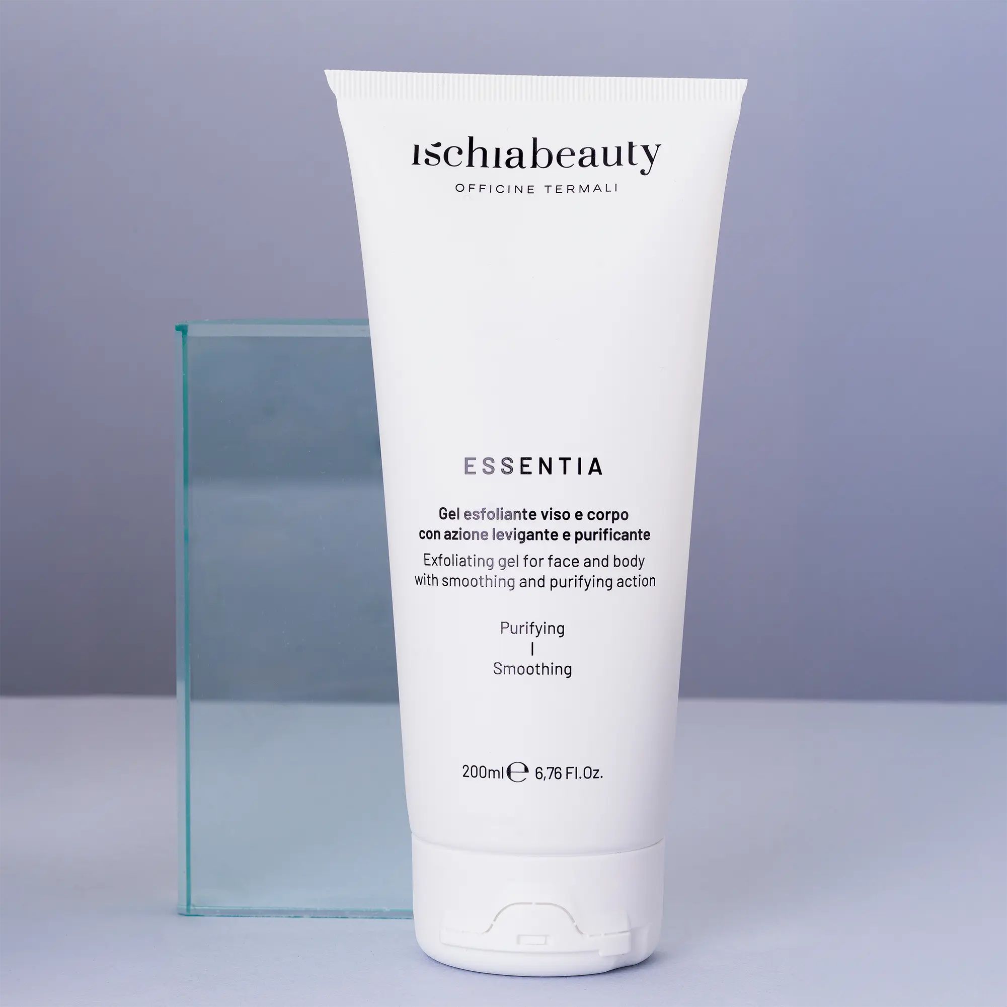 Weiße Tube mit Produktbeschriftung. Text: Ischiabeauty, Essentia, Gel esfoliante viso e corpo. Auf blauem Hintergrund, neben Glasobjekt.