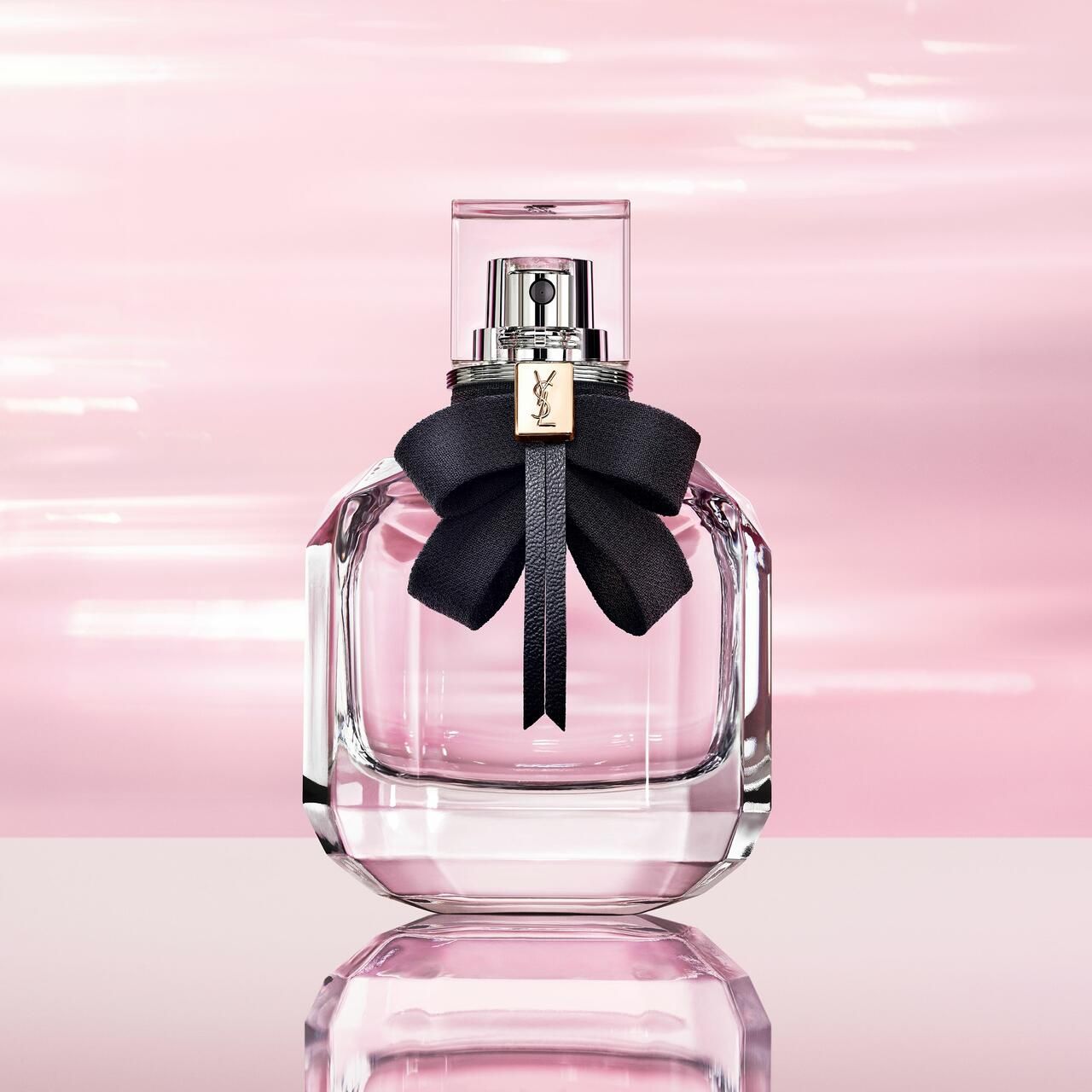 Parfümflakon mit schwarzer Schleife. Glasflakon mit rosa Flüssigkeit, auf rosa Untergrund.