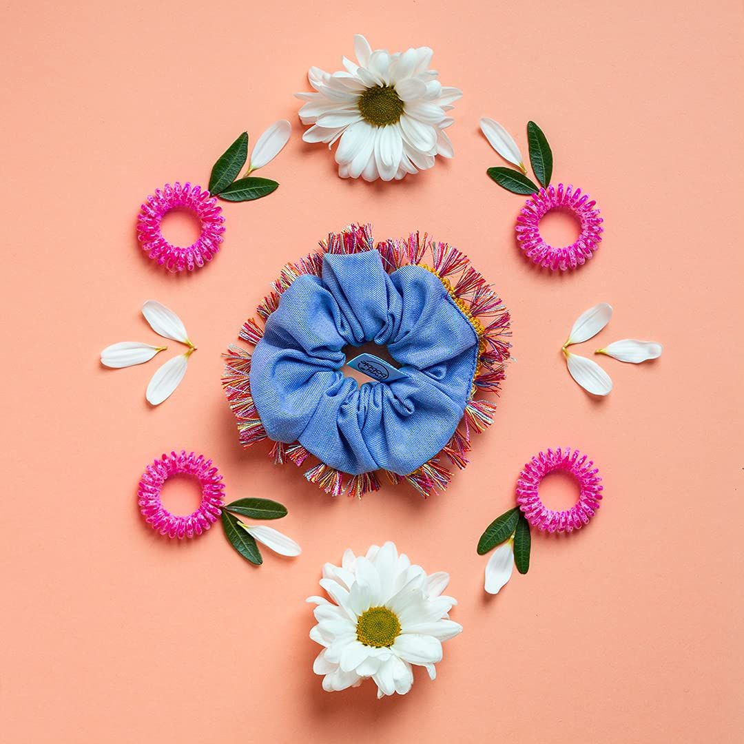 Hellblauer Hola Lola Sprunchie Scrunchie mit bunten Fransen, umgeben von Blumen.