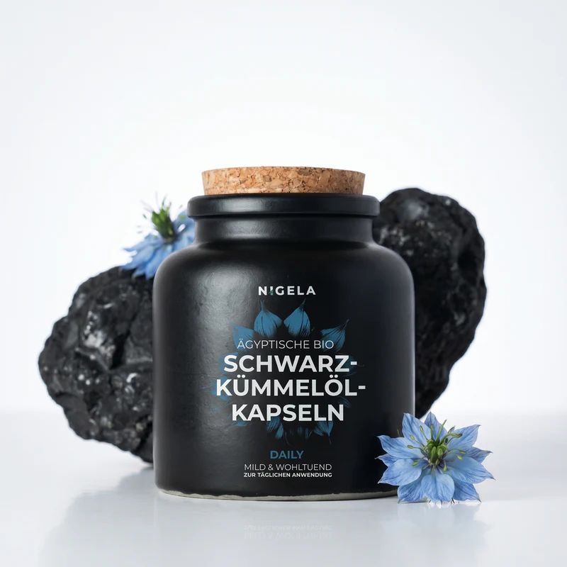 Schwarzkümmelöl Kapseln in schwarzer Keramikdose mit Korkverschluss, umgeben von Steinen und blauen Blüten.