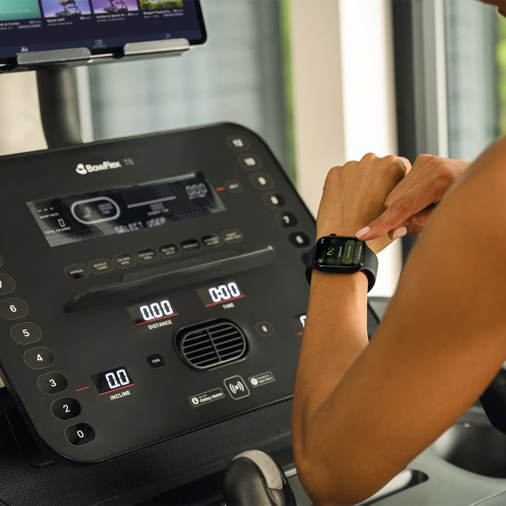 Nahaufnahme der Konsole eines Laufbands. Eine Person tippt auf eine Smartwatch.