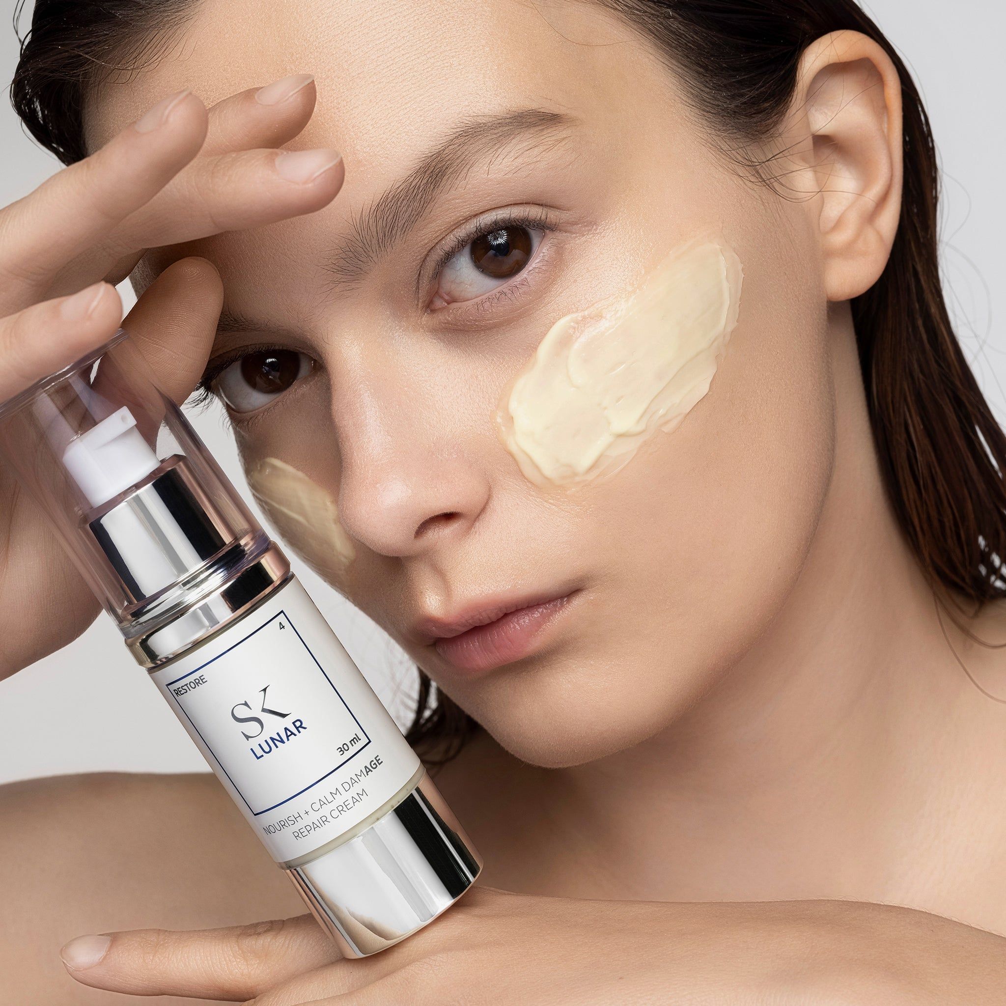 Donna con crema sul viso. Erogatore di crema in mano. Scritta: SK Lunar, 30 ml, Nourish + Calm Damage Repair Cream.