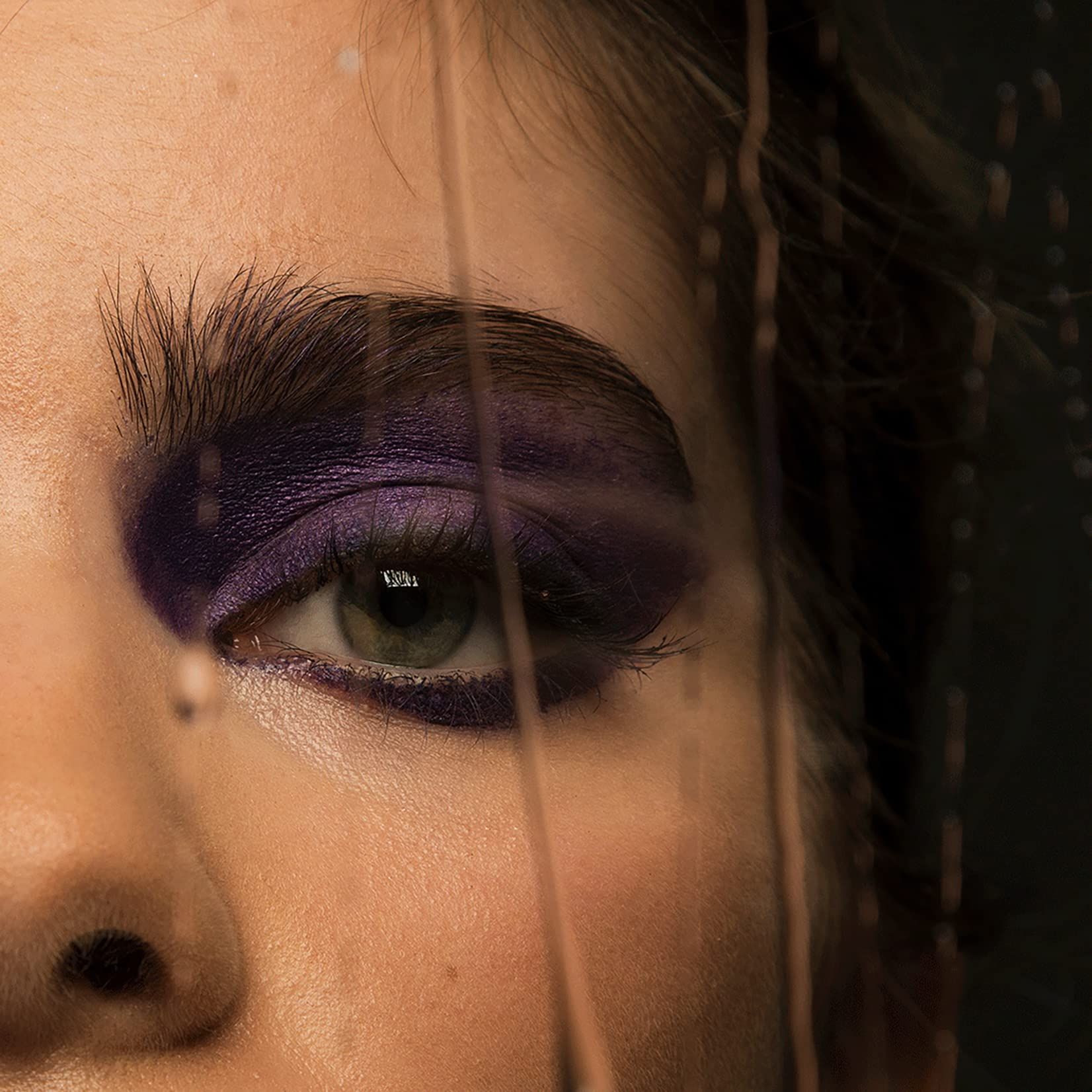 Auge mit violettem Lidschatten. Augenbraue. Teilweise verdeckt durch eine transparente Oberfläche.