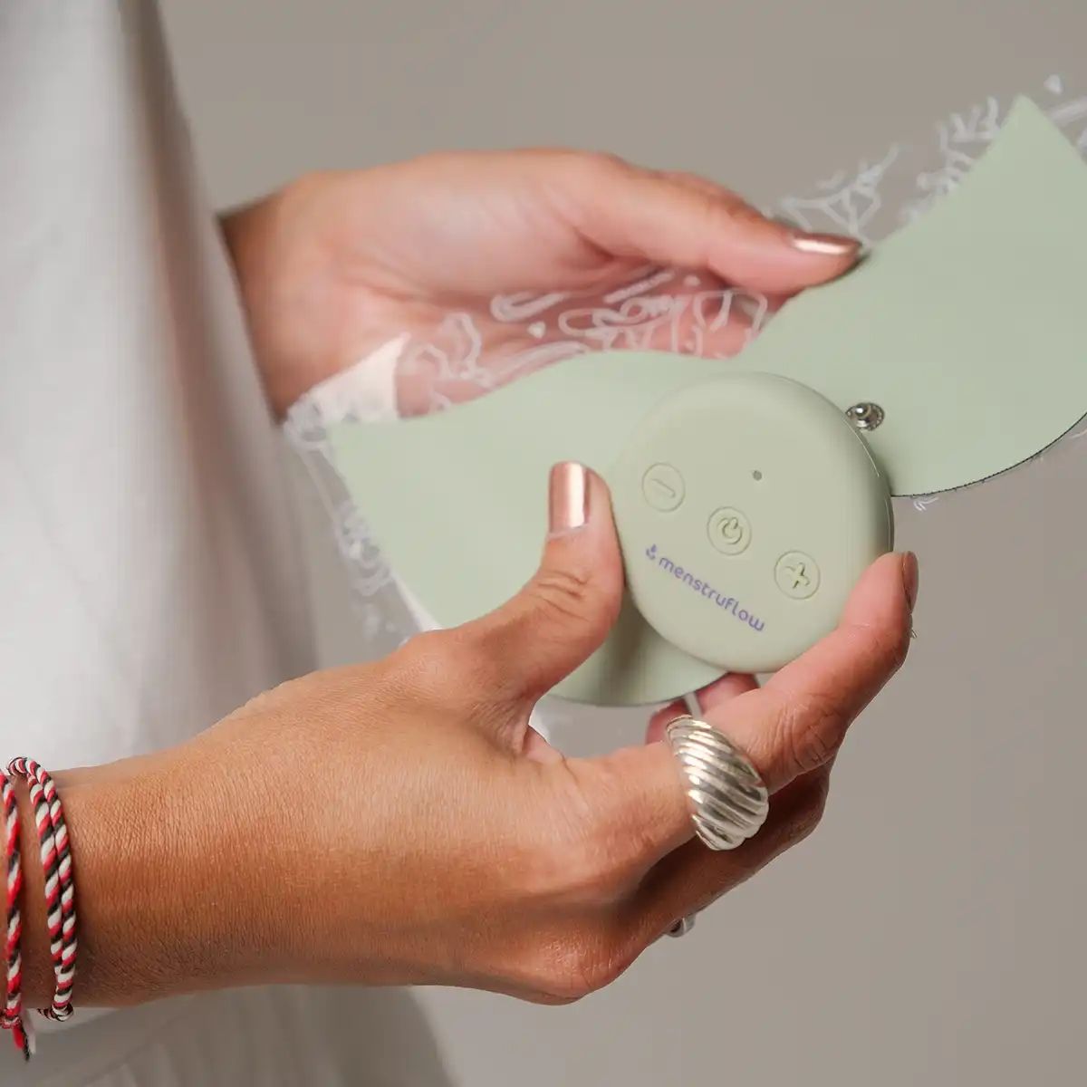 Hände halten ein grünes Flow-Pad und das Steuergerät mit Tasten und "menstruflow"-Logo.