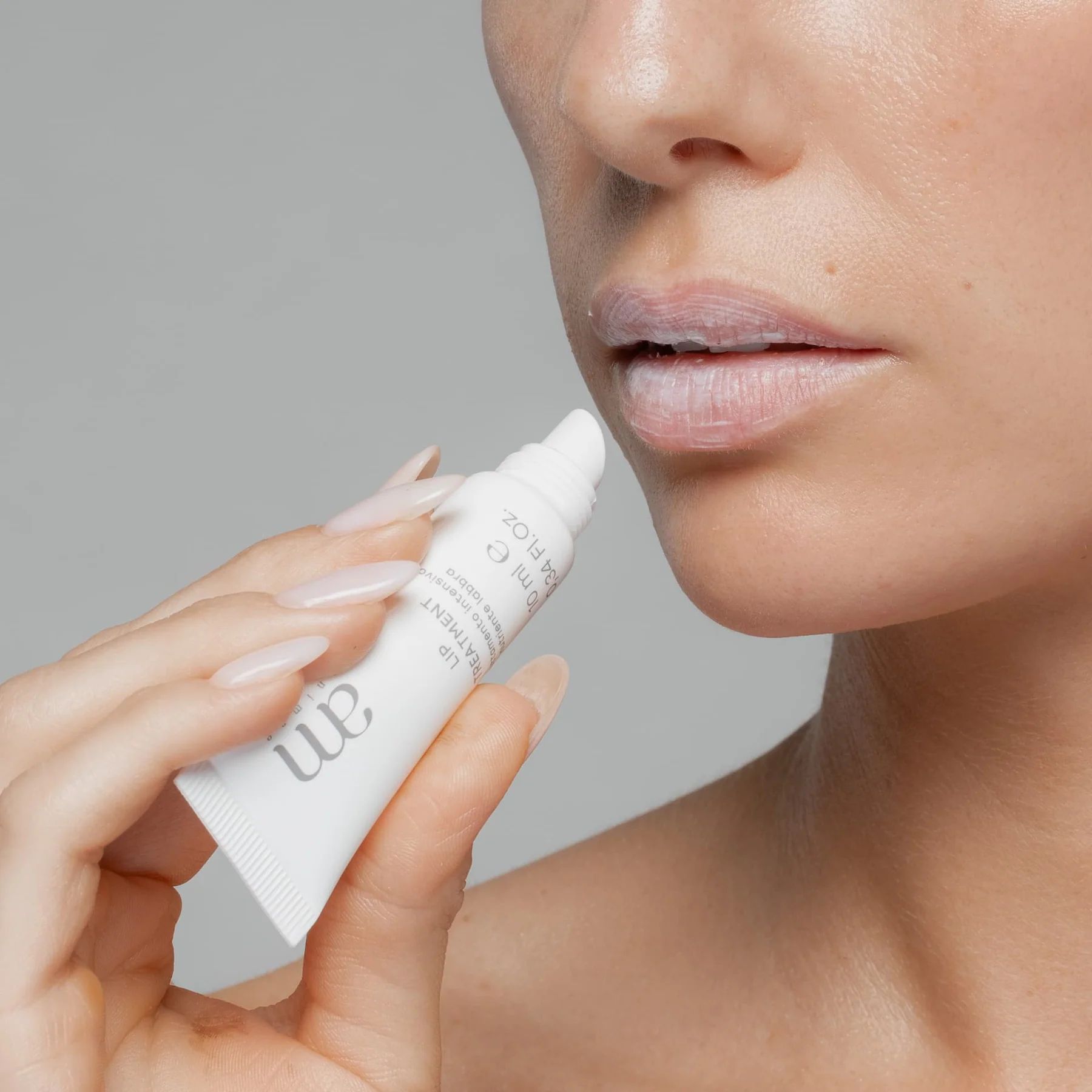 Una persona applica un prodotto da un tubetto bianco con il logo "am" sulle labbra. Il tubetto indica "10 ml e".