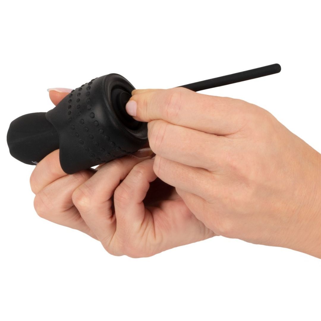 Eine Hand hält einen schwarzen Masturbator, die andere platziert einen Dilator. Das Produkt hat eine strukturierte Oberfläche.
