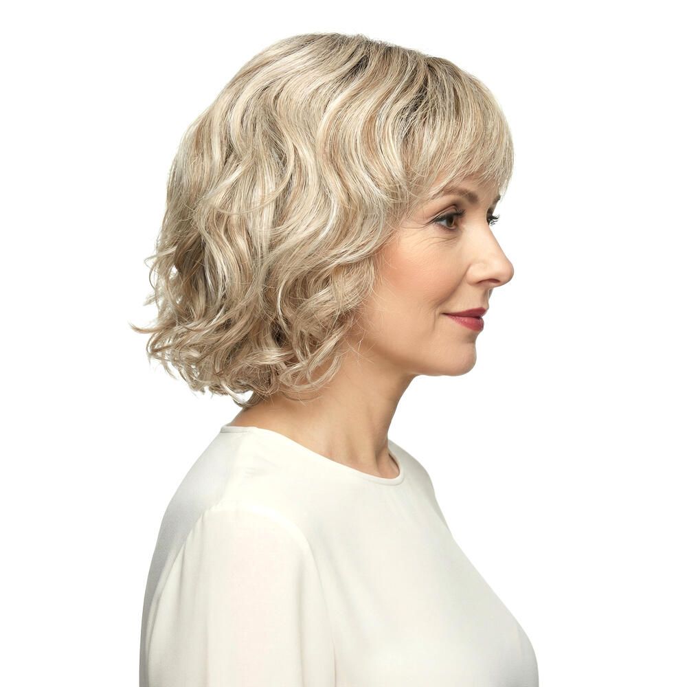 Perücke Capri von DELUXE. Blond gewellt, mit Pony. Frau mit Perücke, Seitenansicht.