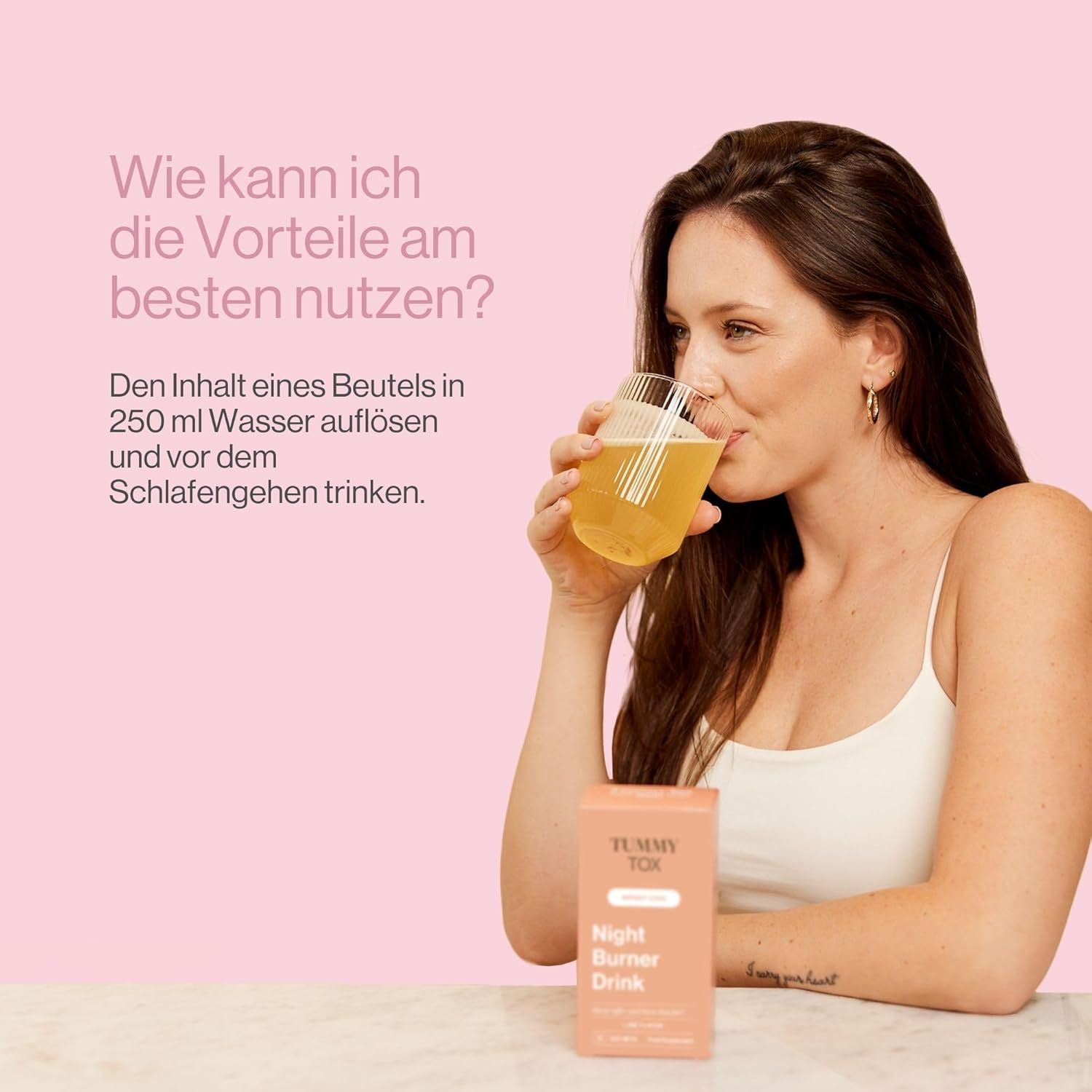 Frau trinkt aus einem Glas. Auf dem Tisch steht eine rosa Schachtel mit "Tummy Tox Night Burner Drink".