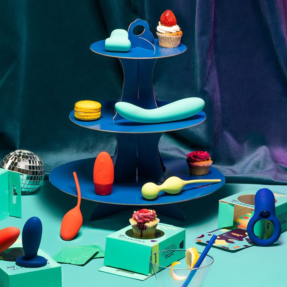 Mehrere Intimprodukte auf einem blauen Tablett. Darunter ein türkisfarbener Dildo, Cupcakes und andere Produkte.
