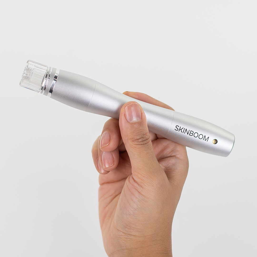Silberfarbener SKINBOOM Hydra Glow Pen in einer Hand gehalten. Markenschriftzug deutlich sichtbar.