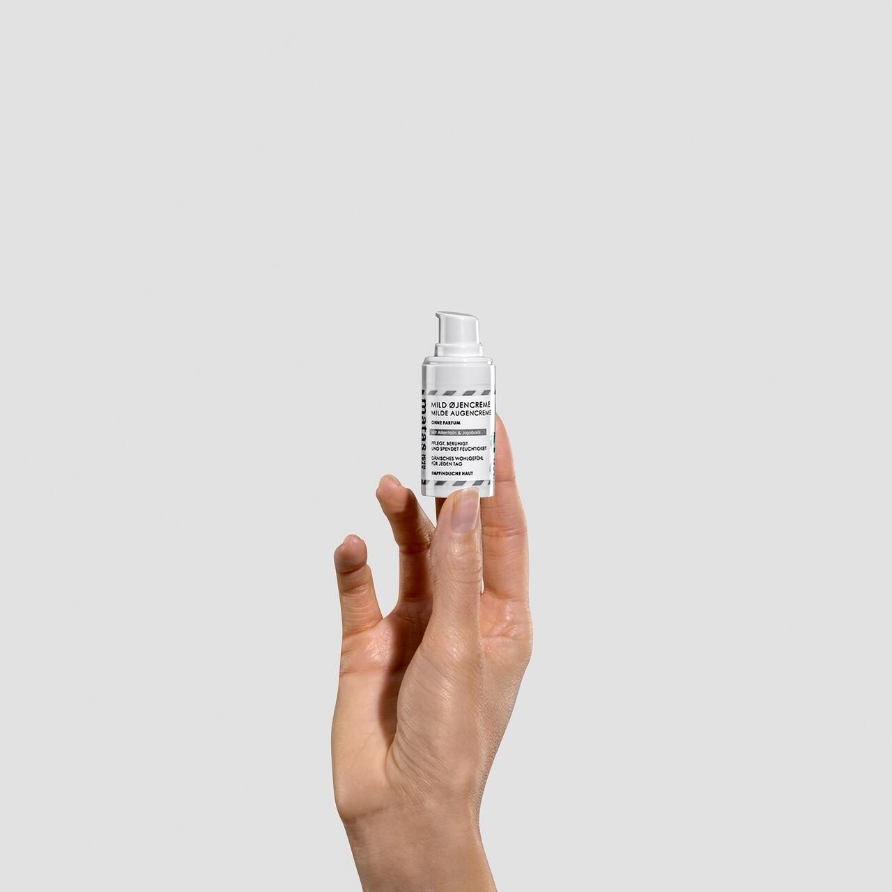 Weißer Spender mit Text. Hand hält Spender. Aufschrift: Milde Augencreme. Ohne Parfum.