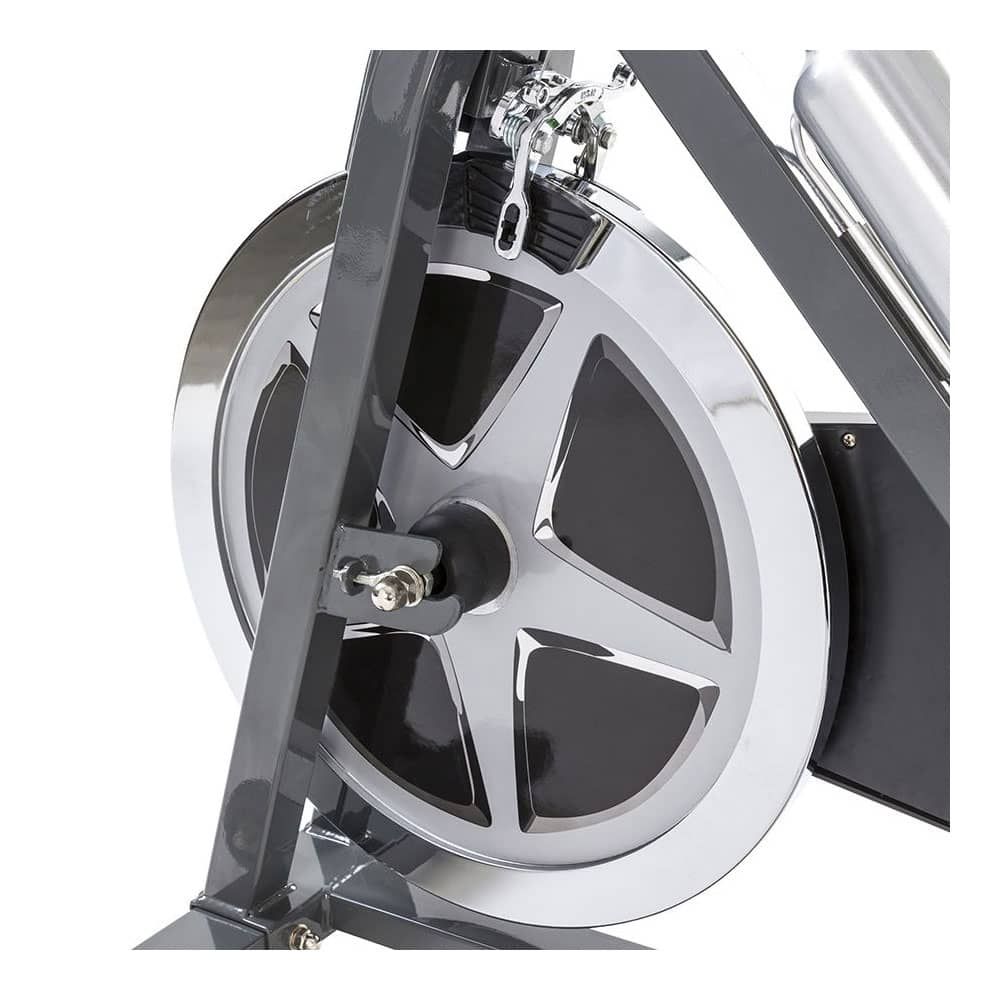 Nahaufnahme des Schwungrads eines Indoor Cycles. Das Rad ist silberfarben und hat eine schwarze Abdeckung. Details der Mechanik sind sichtbar.