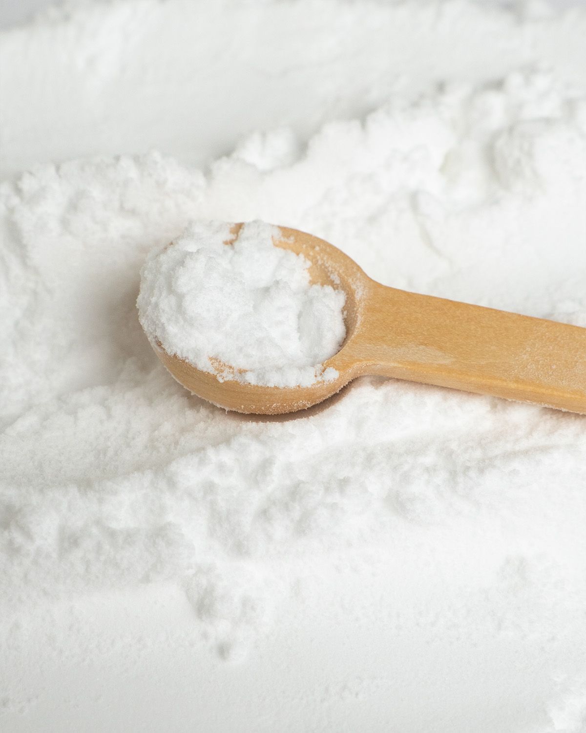 Nahaufnahme von feinem weißem Sucralose-Pulver mit einem kleinen Holzlöffel.