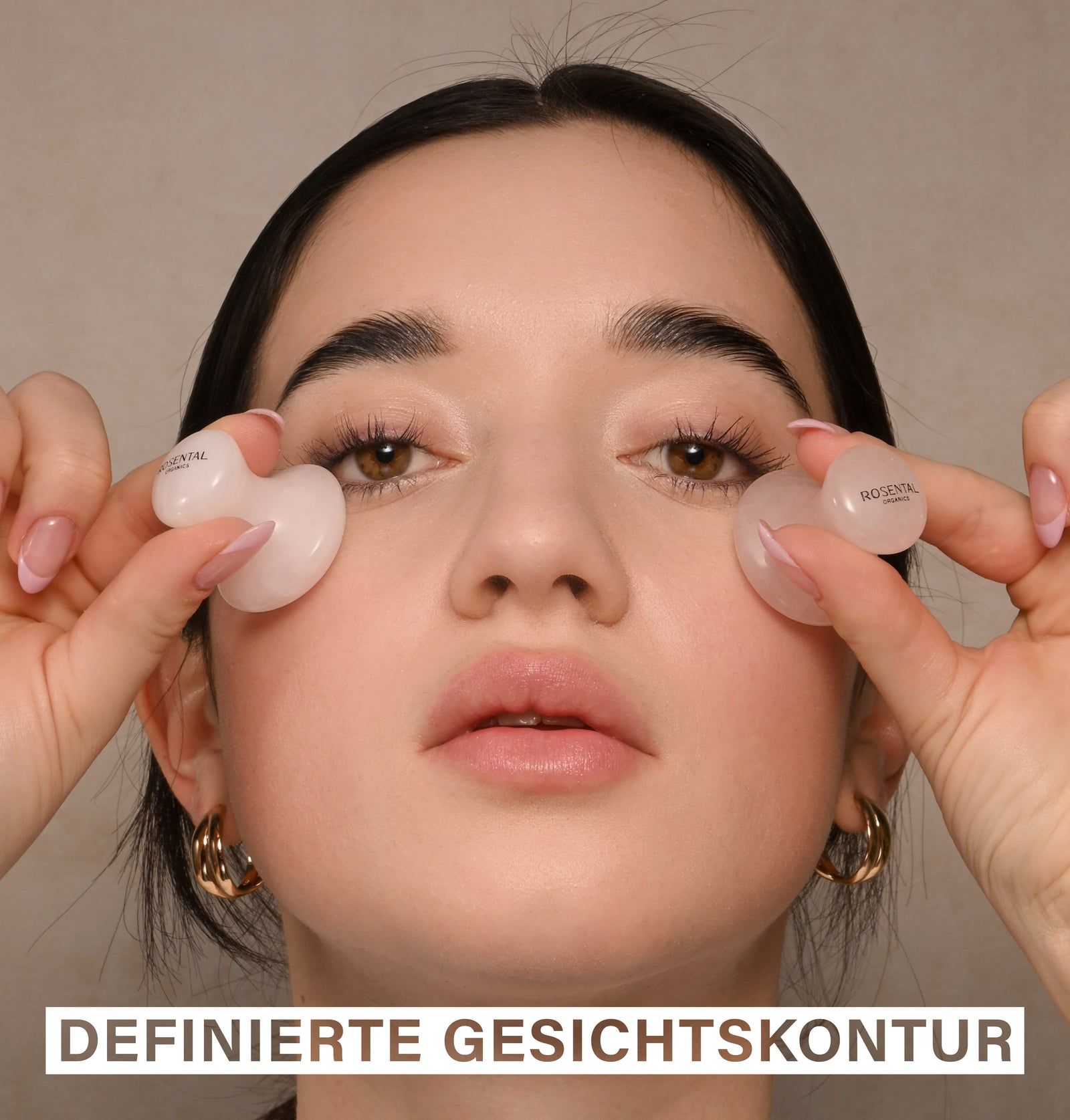Frau hält zwei rosafarbene Eye Flowies Rose Quartz vor ihren Augen. Auf den Flowies ist der Markenname zu sehen.