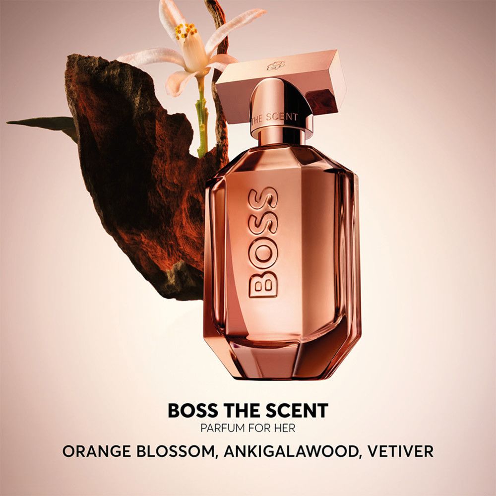 Parfümflakon, kupferfarben, achteckig. BOSS The Scent Parfum for Her. Blüten und Holz im Hintergrund.