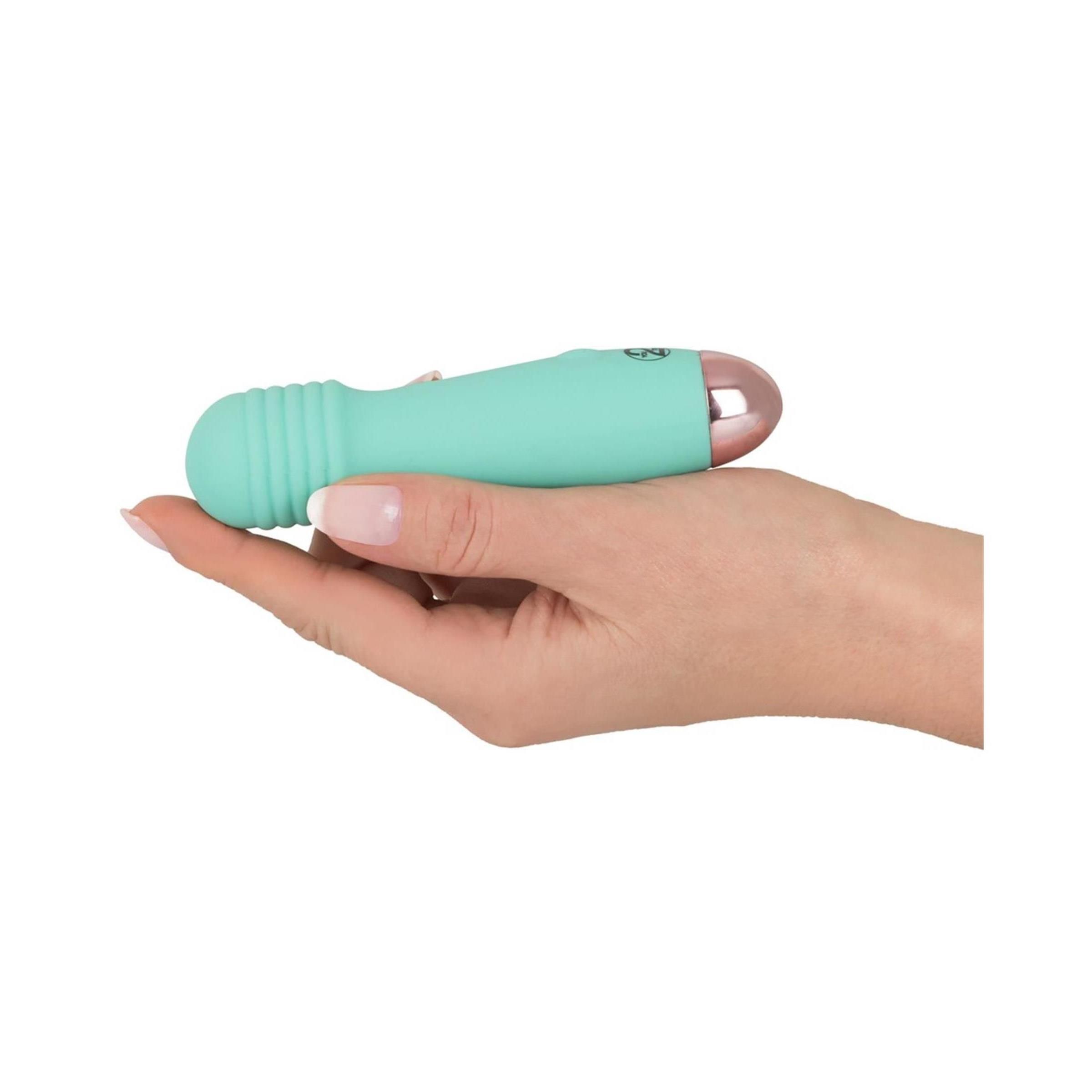 Minivibrator, mintgrün, liegt in einer Hand. Die Spitze ist rosa. Der obere Teil hat Rillen. Ein Knopf ist sichtbar.