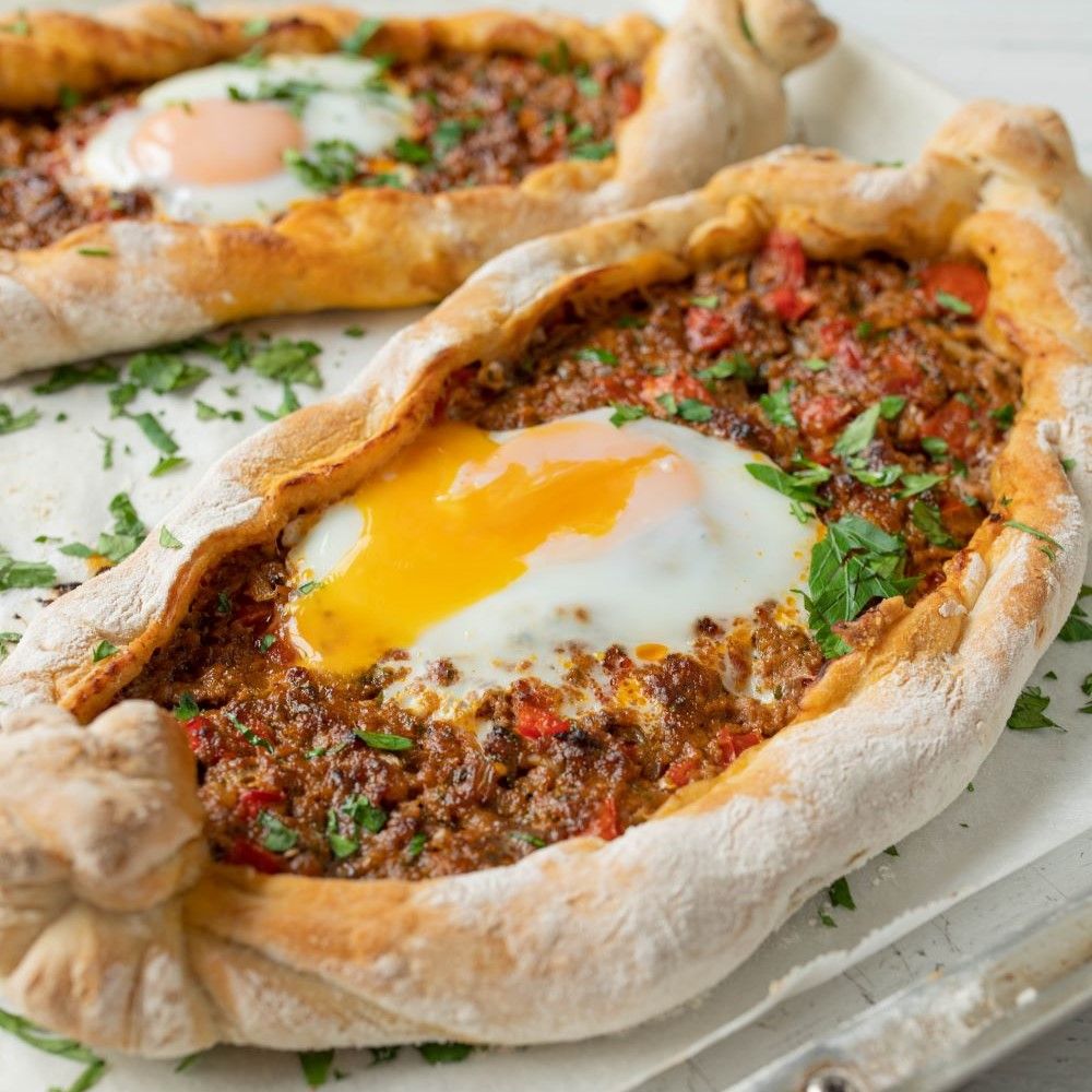 Zwei Pide-Gerichte mit Hackfleisch, Tomaten, Paprika und Ei. Auf hellem Untergrund.