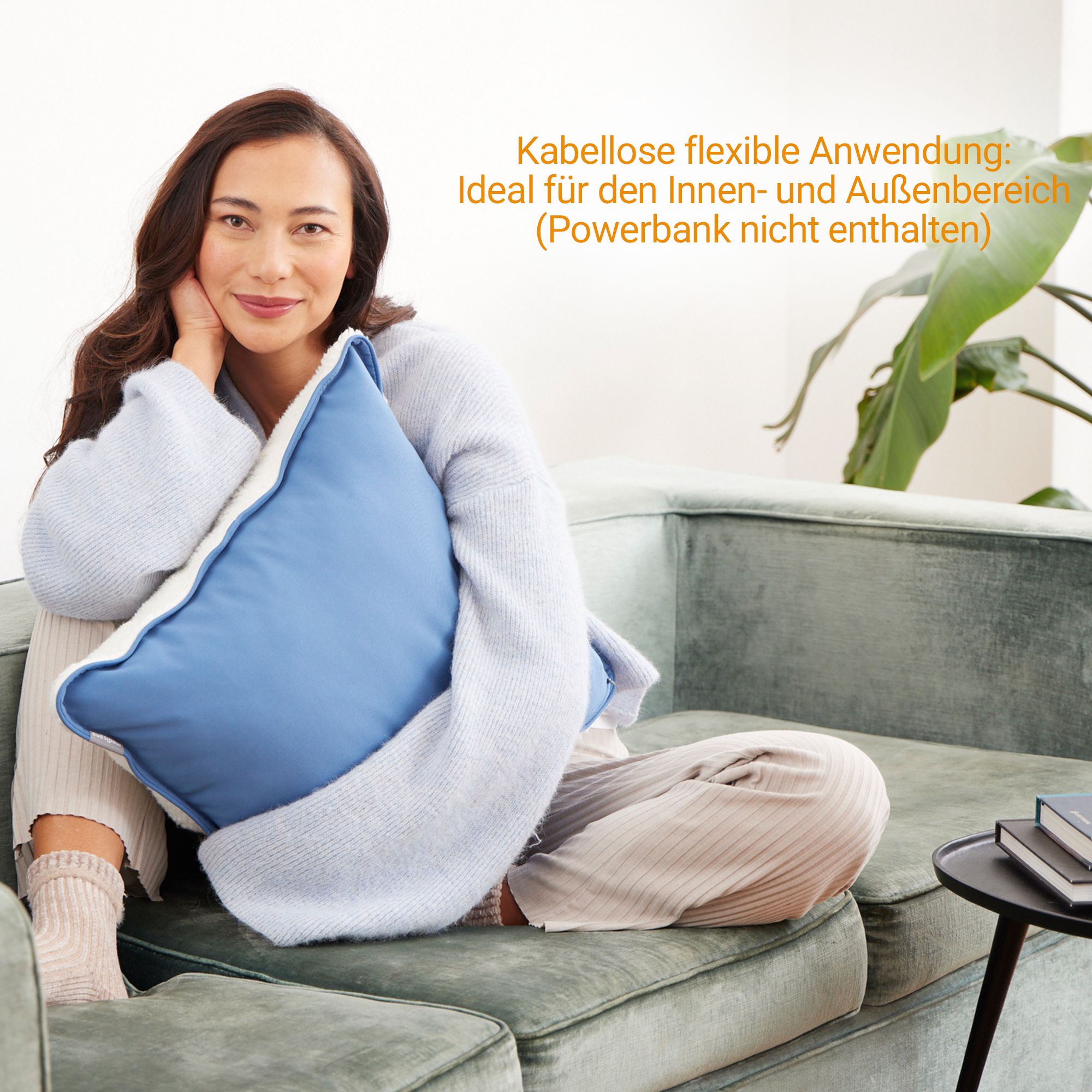 Frau hält ein blaues Heizkissen, das auf einem Sofa liegt.