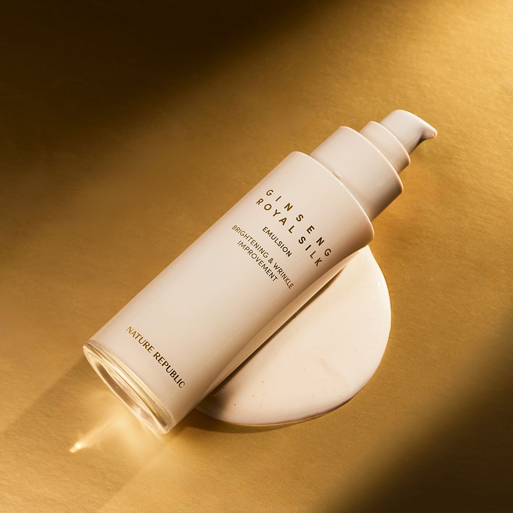 Beige Flasche mit Pumpe, 'Ginseng Royal Silk Emulsion' Schriftzug. Liegt auf cremiger Substanz. Goldener Hintergrund.