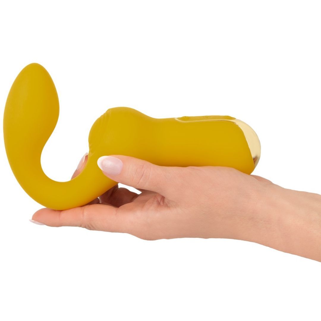 Gelber Vibrator, gehalten in einer Hand. Geschwungene Form mit abgerundetem und länglichem Ende. Goldfarbener Akzent.
