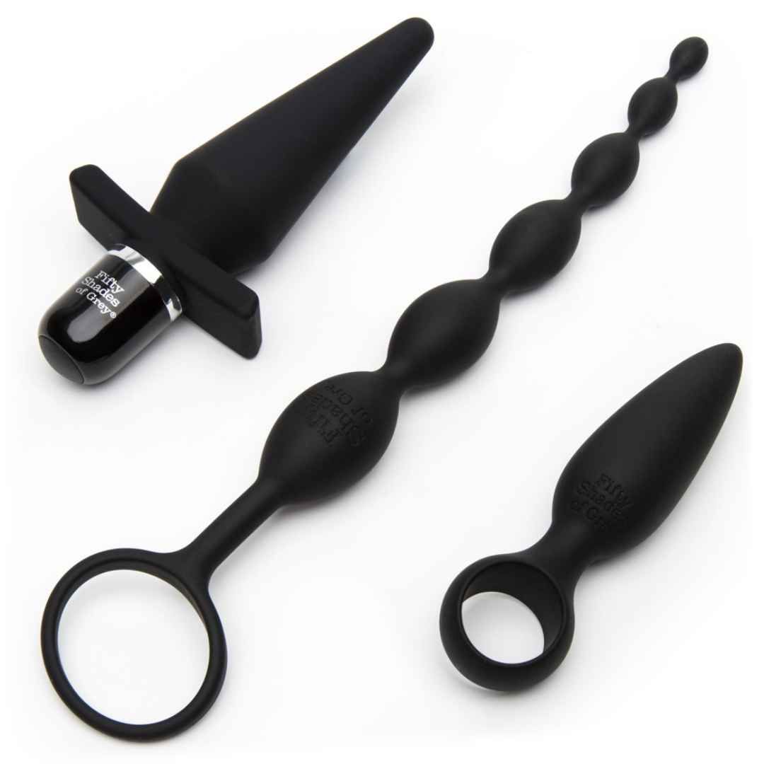 Drei schwarze Intimprodukte: Analplug, Analkette und Analplug mit Ring. Alle mit Fifty Shades of Grey-Logo.