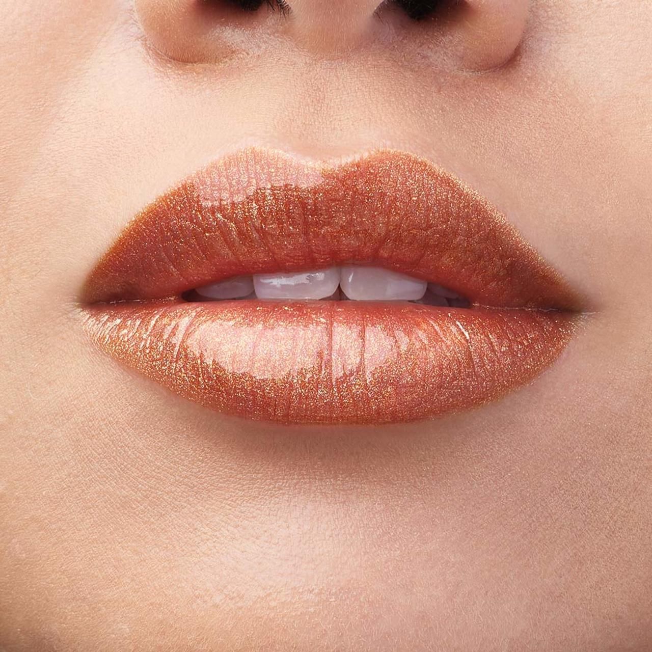 Nahaufnahme von Lippen, bedeckt mit glänzendem, bronzefarbenem Lippenlack. Sichtbare Zähne.