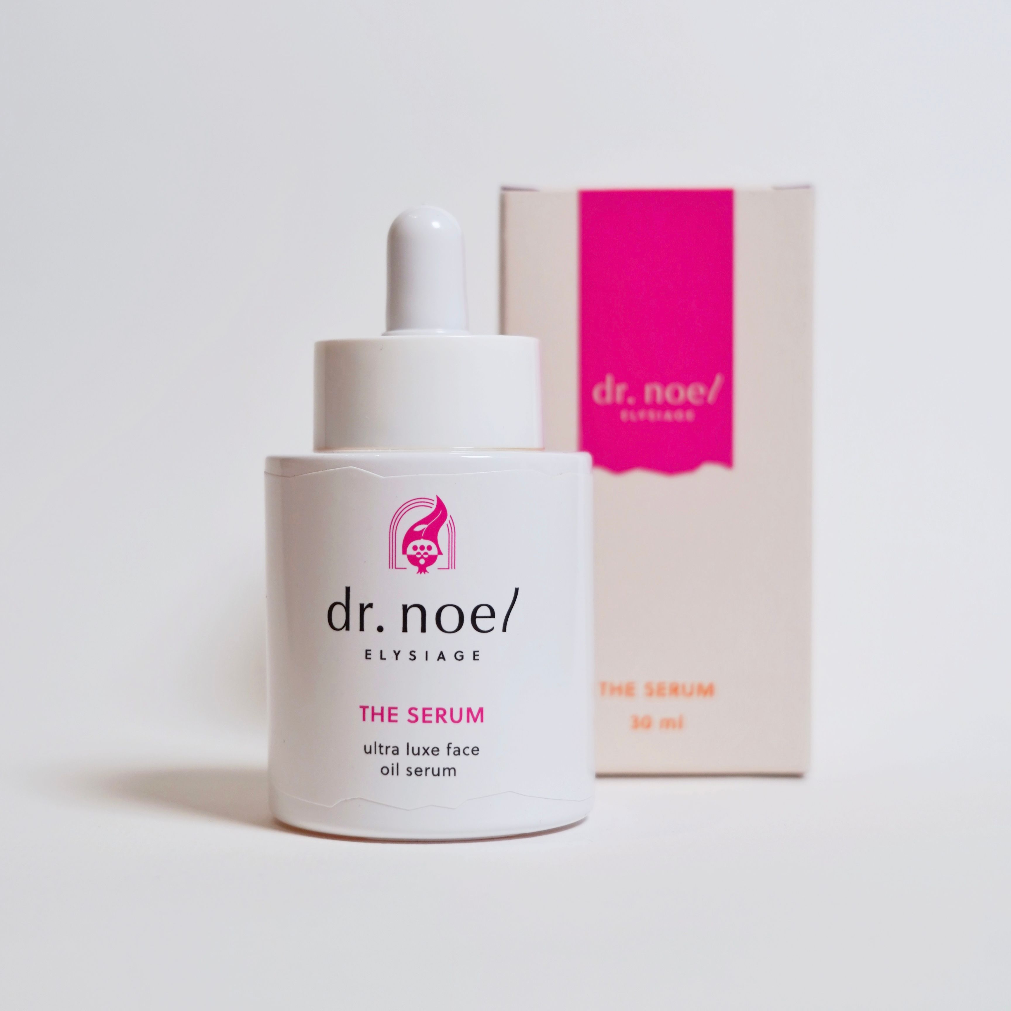 Weiße Flasche mit Serum und Verpackung. Aufschrift: dr. noel/ ELYSIAGE, THE SERUM, ultra luxe face oil serum. Rosa Akzente.
