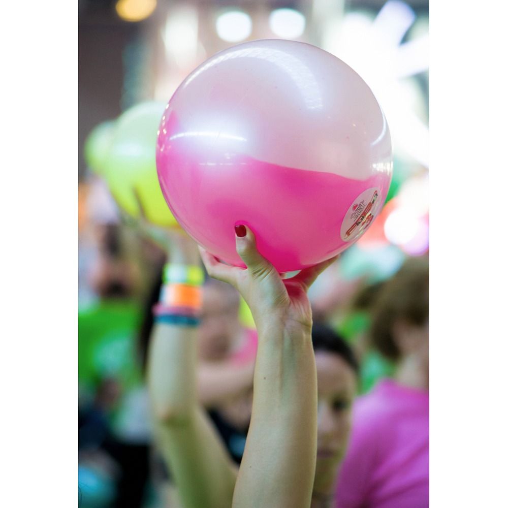 Person hält eine zweifarbige pink-weiße Gewichtsball in die Höhe. Andere Bälle im Hintergrund.