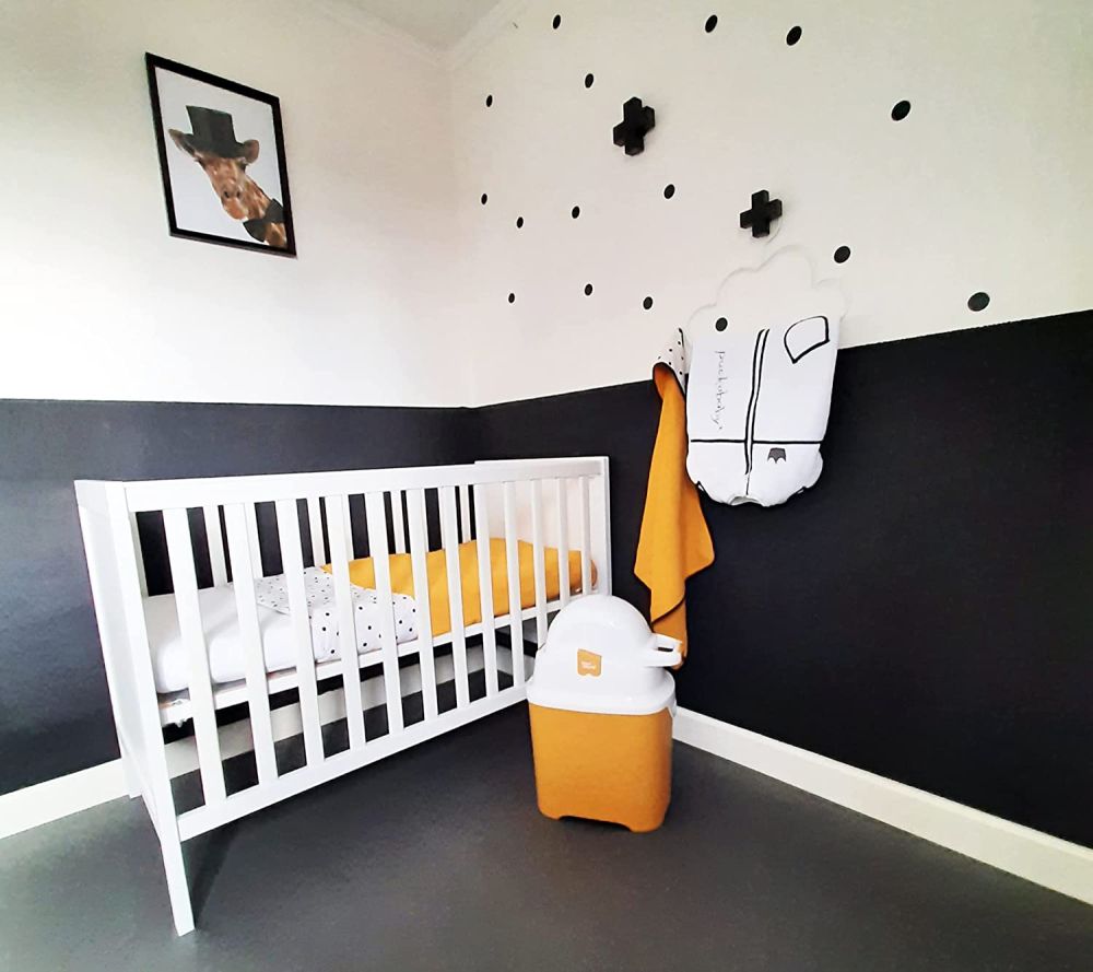 Gelber Windeleimer in einem Kinderzimmer. Weißer Deckel mit Ausguss. Aufschrift: Diaper Champ.