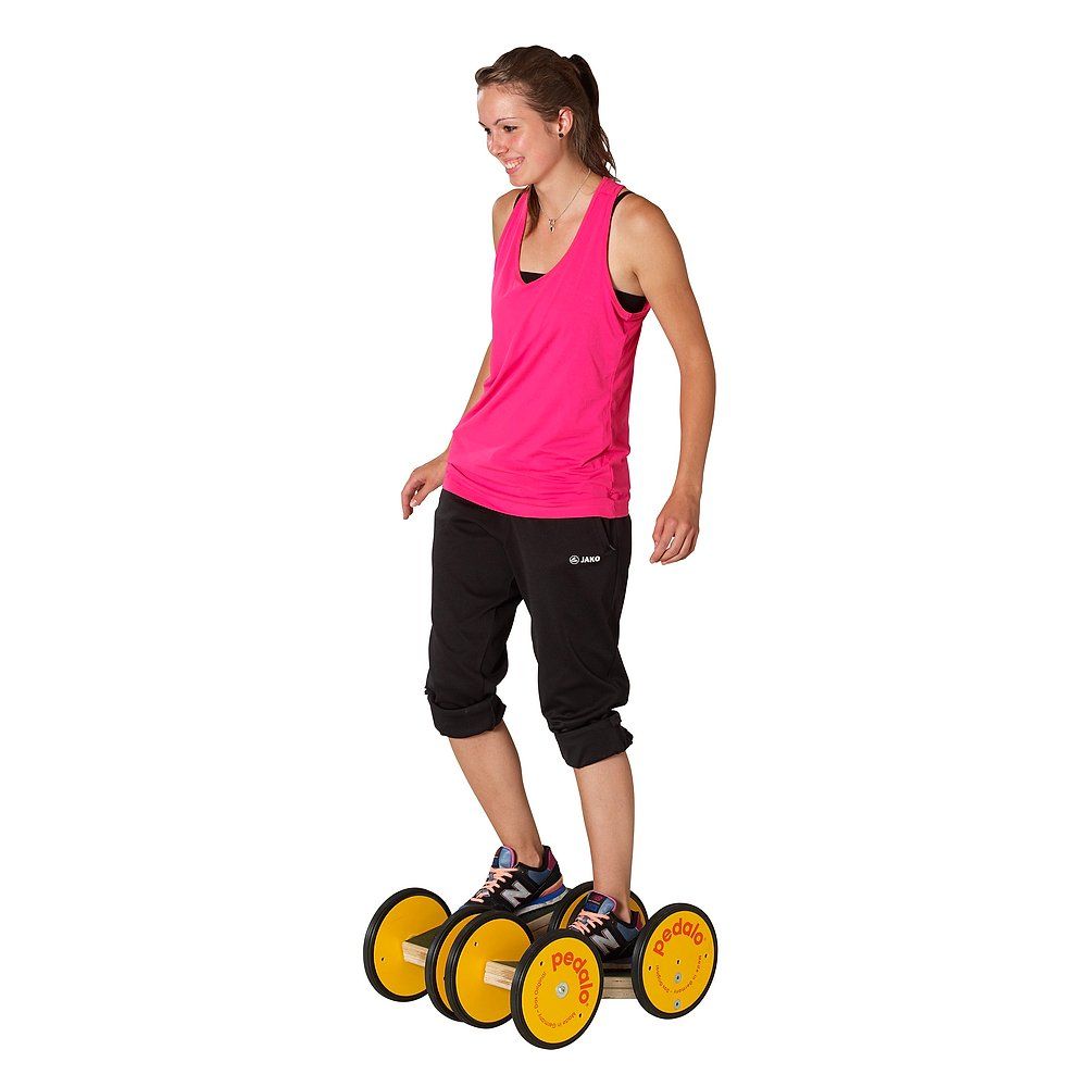 Frau auf Pedalo Koordinationstrainer. Gelbe Räder, Holzrahmen. Aufschrift: Pedalo. Die Person steht auf dem Gerät.