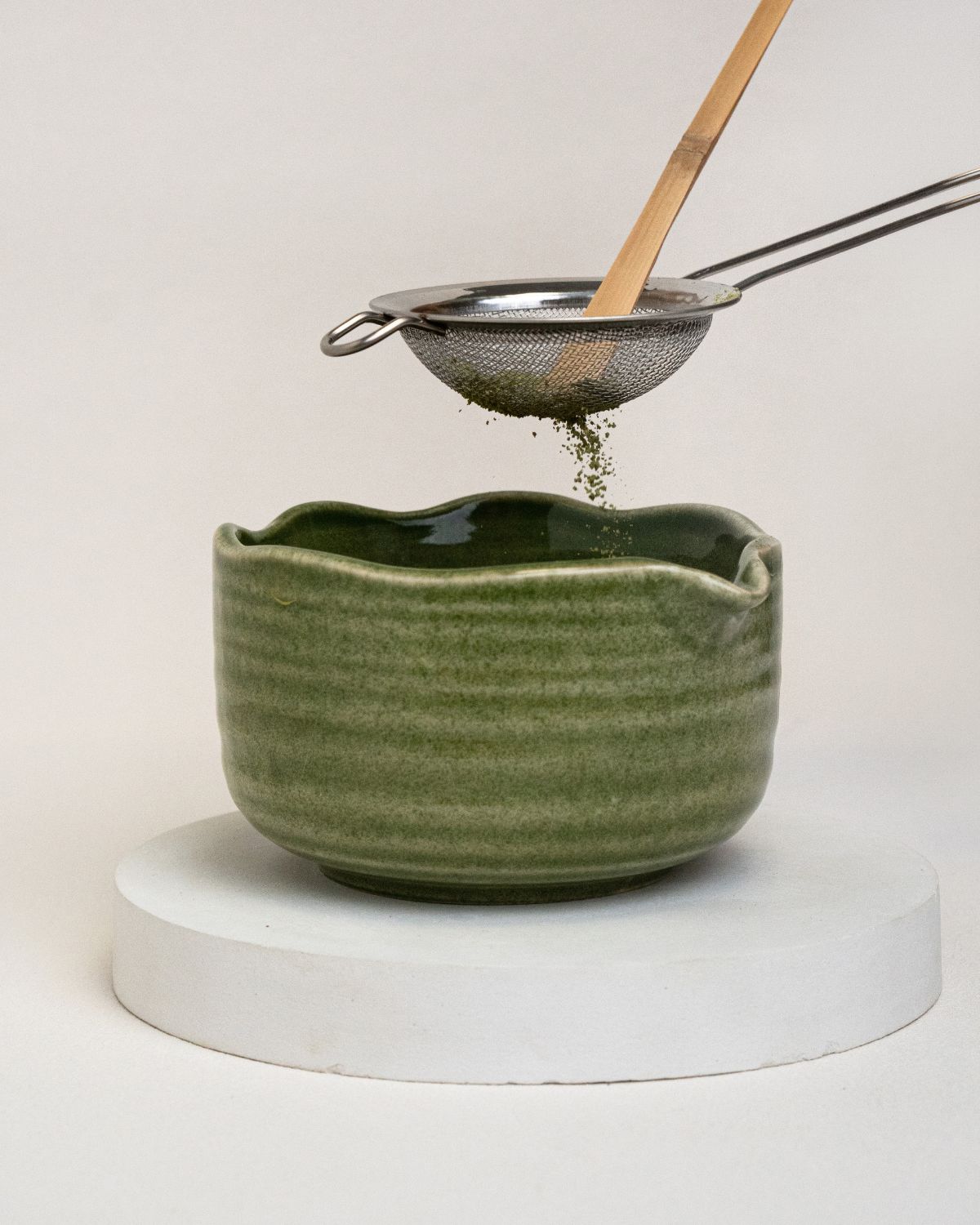 Grünes Keramikgefäß, Sieb und Bambuslöffel. Matcha-Pulver wird in die Schale gesiebt.