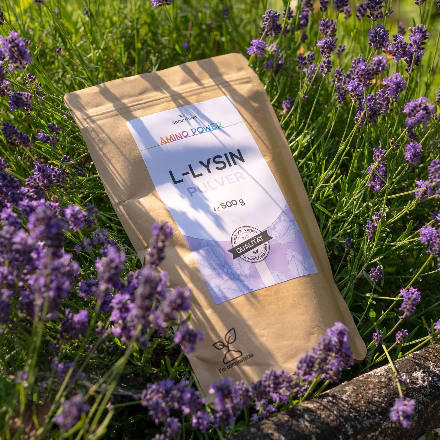 Beutel mit L-Lysin Pulver, 500g. Braune Verpackung mit weißem Etikett, umgeben von Lavendelblüten.