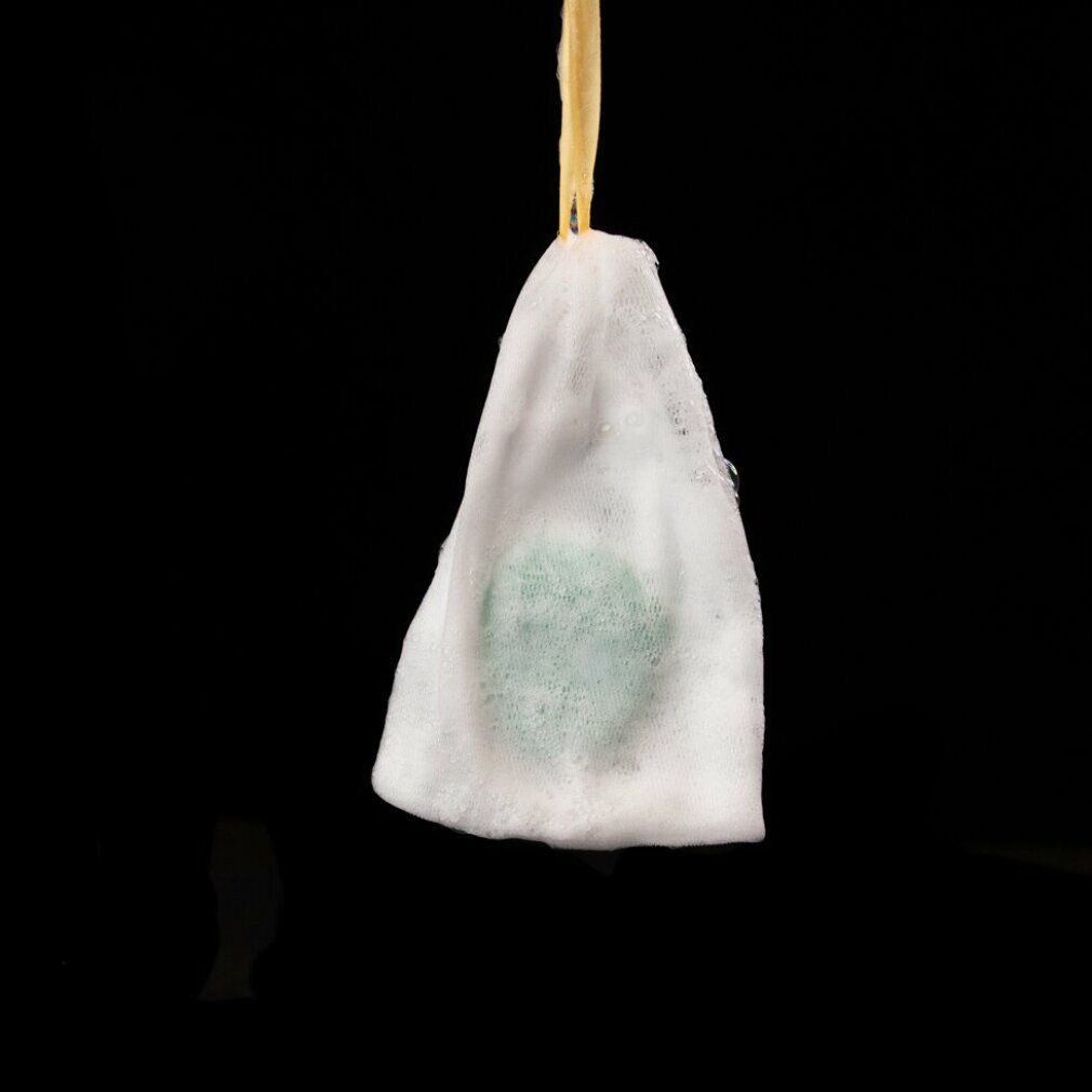 Grünes Shampoo-Bar in einem Schaumstoffbeutel, an einem Faden hängend. Schwarzer Hintergrund.