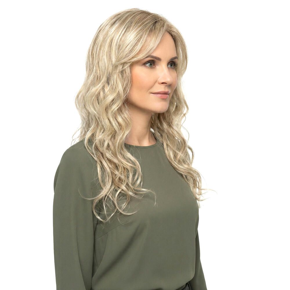 Blond gewellte Perücke mit Pony, Dreiviertelansicht. Die Frau trägt ein grünes Oberteil. Hintergrund weiß.