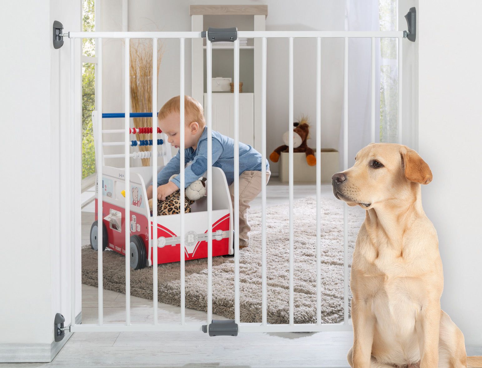 Türschutzgitter im Einsatz. Kind spielt mit Spielzeug, Hund sitzt daneben. Weißes Gitter, graue Befestigungen.