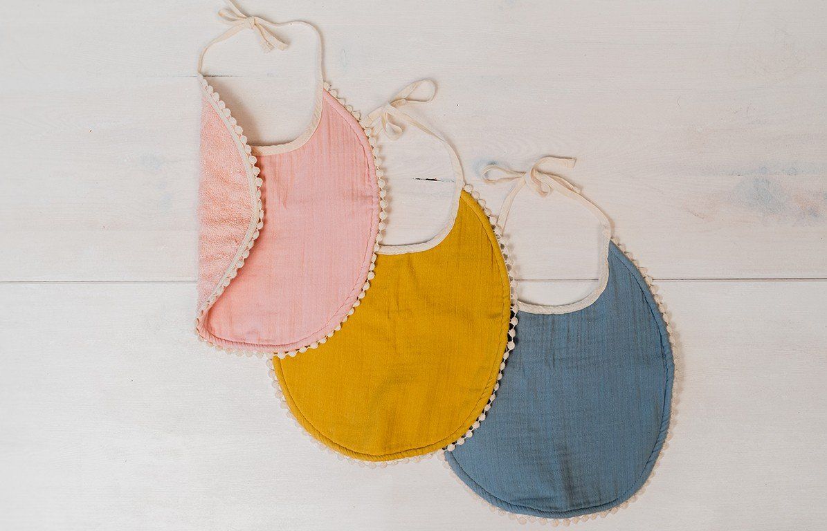 Drei Lätzchen in Rosa, Gelb und Blau. Runde Form, Spitze, Bindebänder.