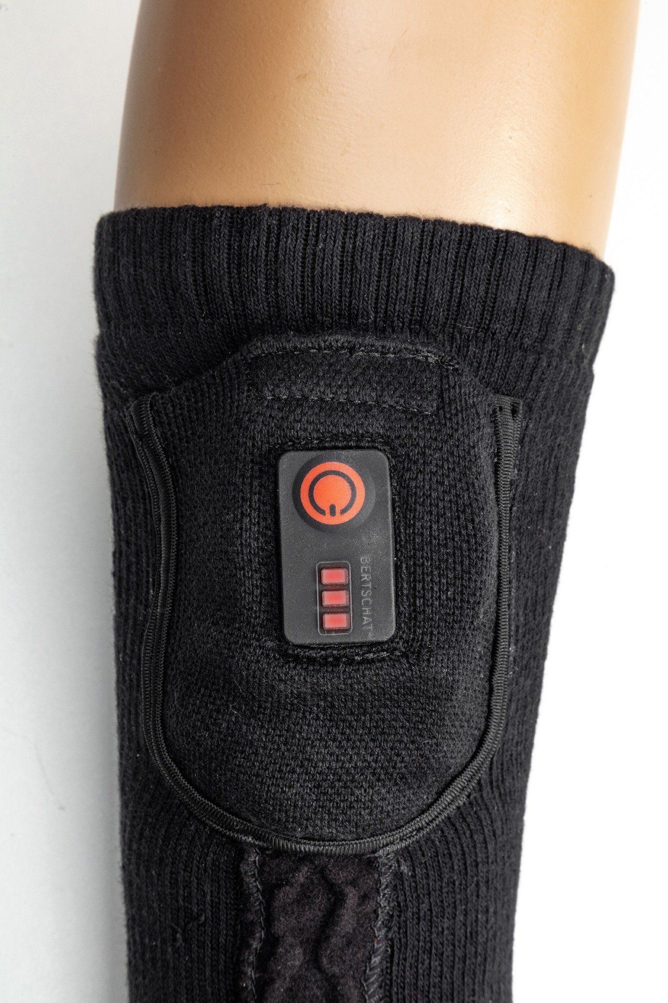 Schwarze Socke mit Heizmodul. Modul mit rotem Bedienfeld und Ladeanzeige. Auf einem Bein präsentiert.