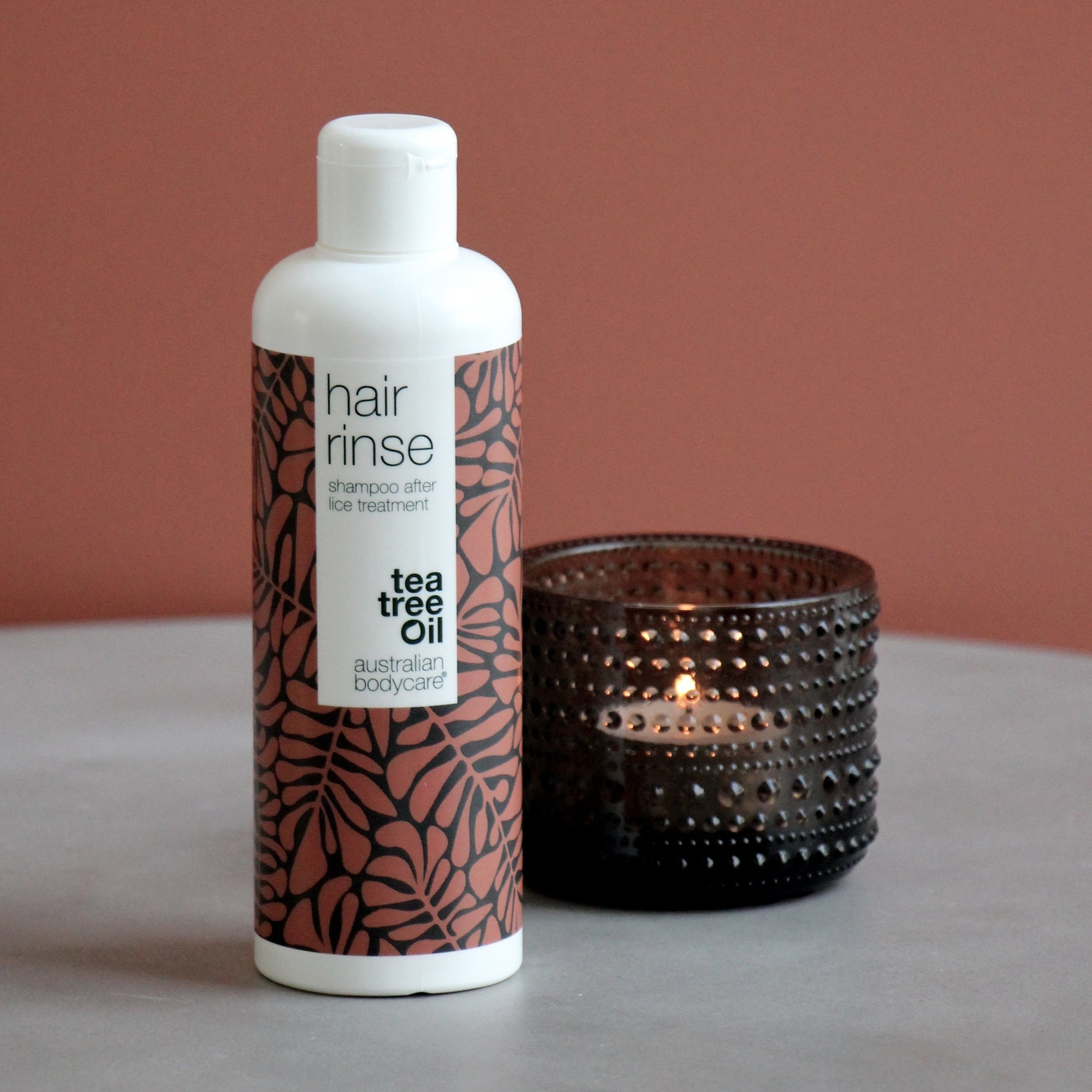 Flasche mit braunem Blattmuster. Aufschrift: hair rinse, shampoo after lice treatment, Tea Tree Oil, australian bodycare. Neben Kerze.